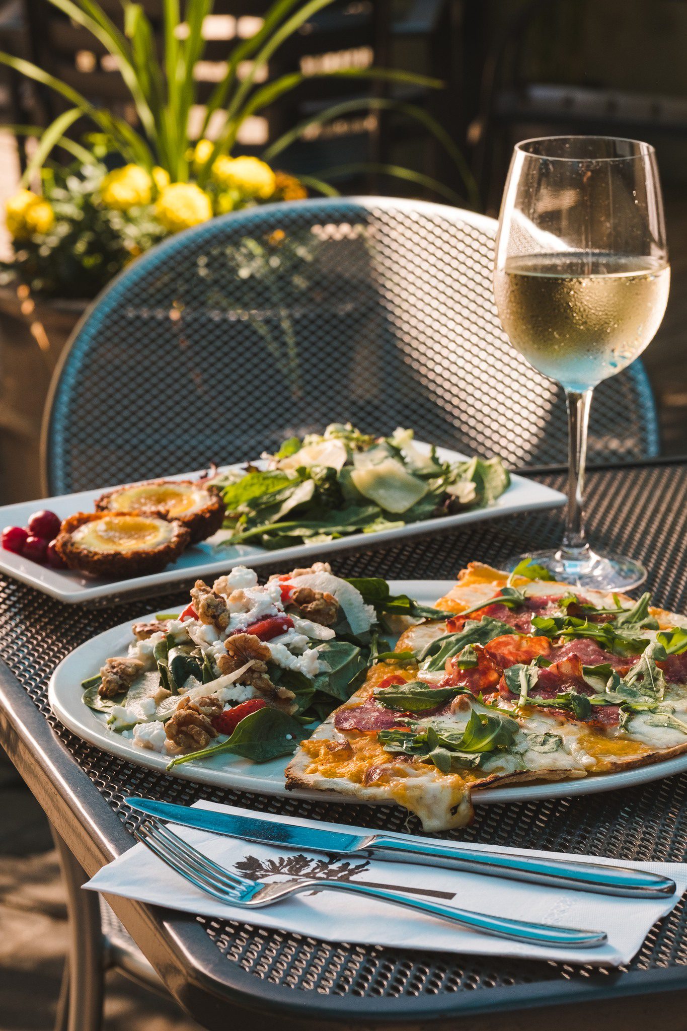 Close up image of wine glass with two plates of food from Miijidaa Café + Bistro