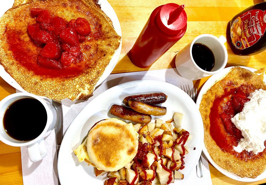 Finnish pancakes with strawberries and whipped cream, coffee and a breakfast sandwich with homefries and coffee