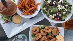Overhead spread of food at The Eddy including Sleeping Giant beer, fried shrimp, greek salad and the eddy burger with sweet potato fries