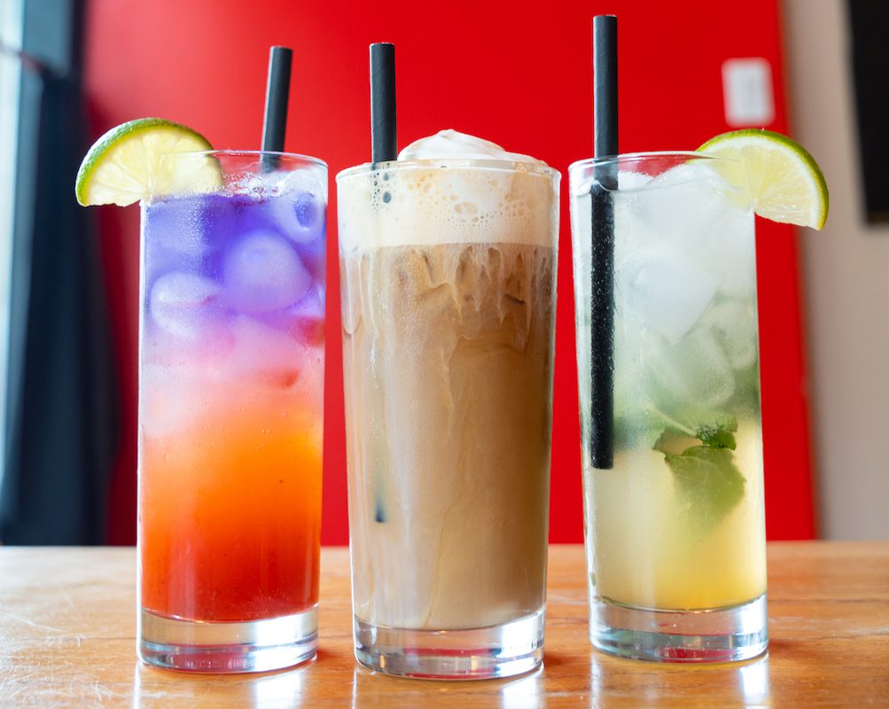 three cocktails lined up in front of a red wall at In Common