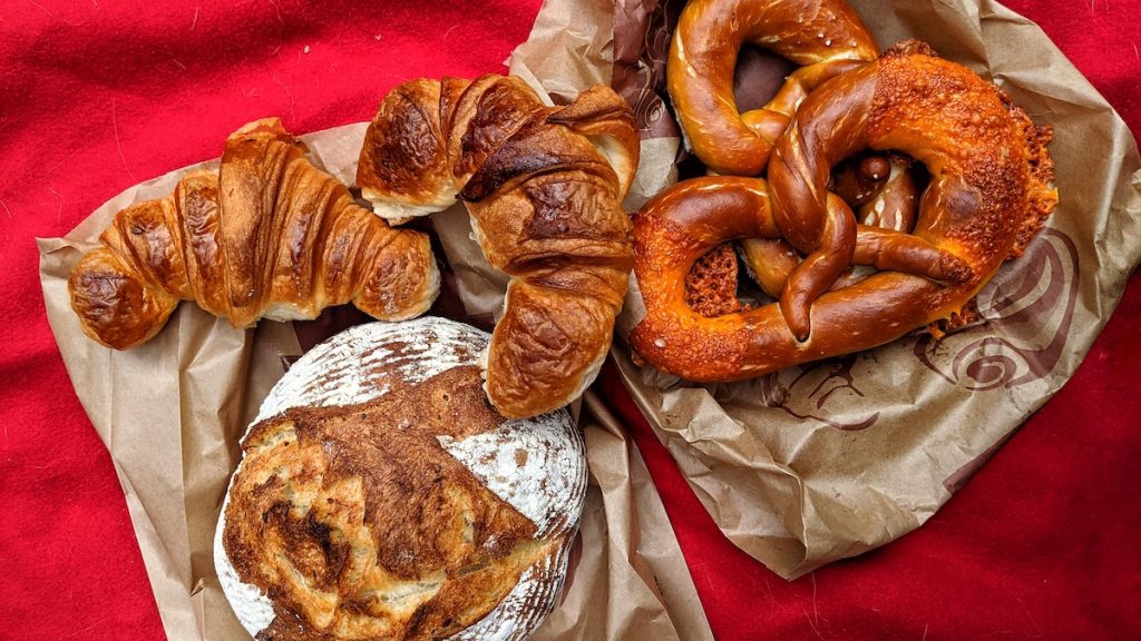 overhead shot of two croissants and a soft-baked pretzel on paper bags and a red table cloth at Mickaels