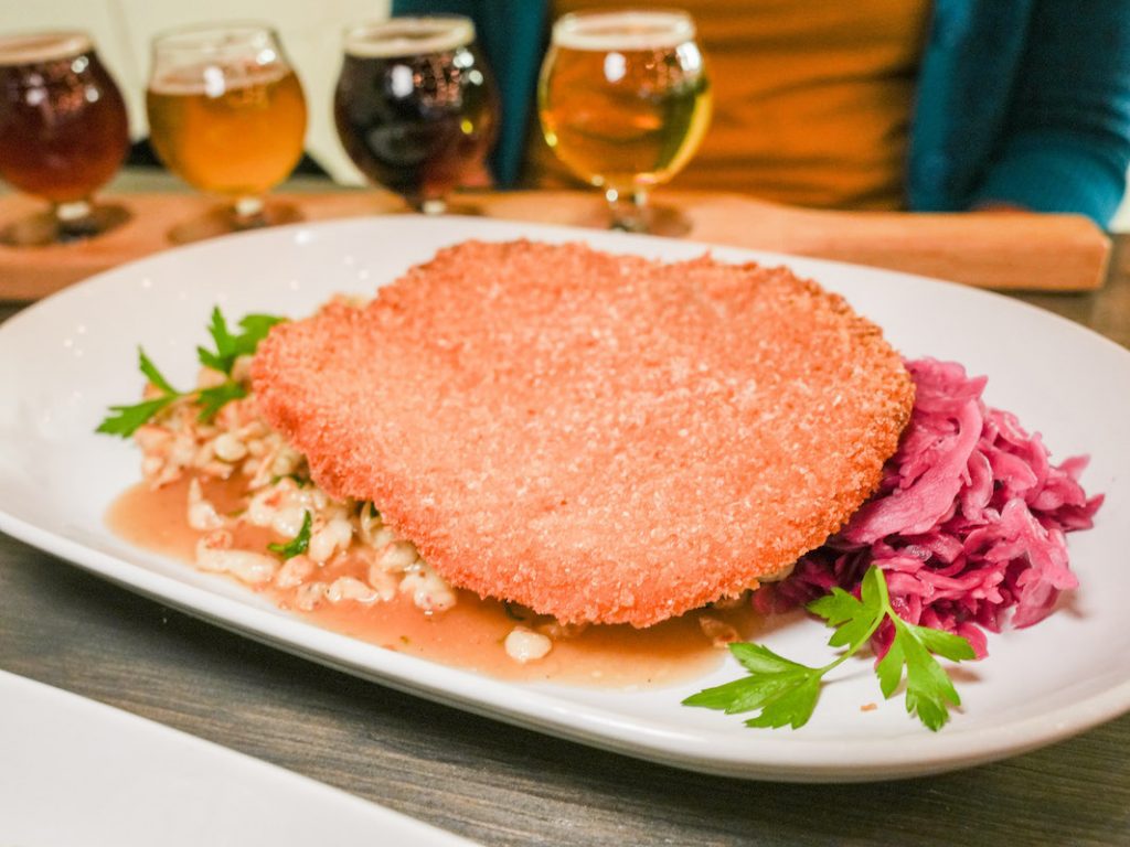 closeup of schnitzel, spaetzle and cabbage at newark brewing co with a flight of beers in the background