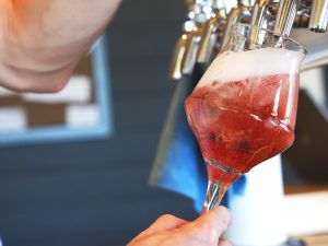 a hot pink sour beer being poured into a stemmed glass from OG bottle shop in galt