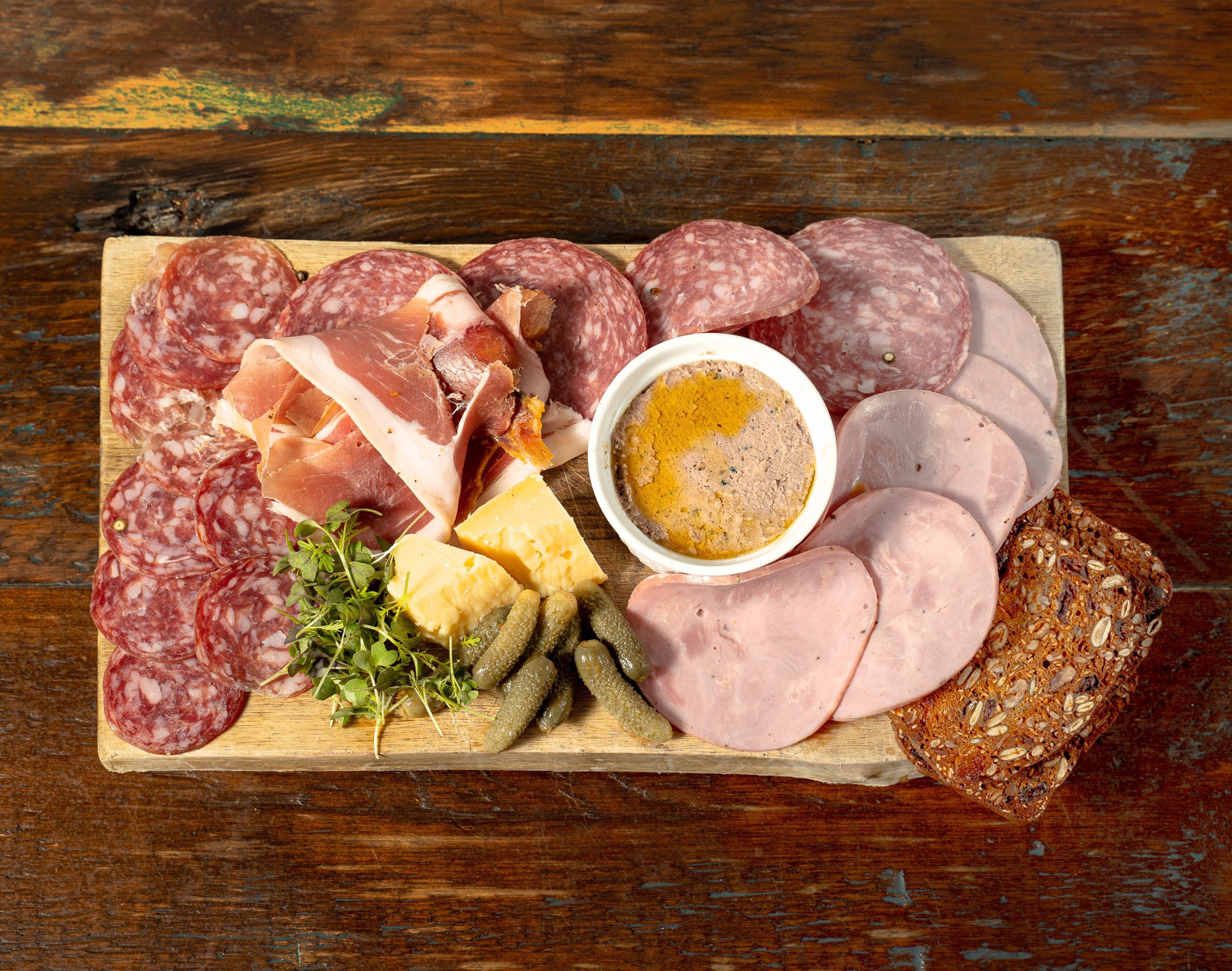 A selection of meats, cheeses, and preserves on a wooden board