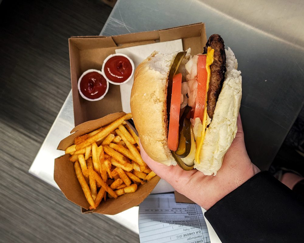 overhead shot of hand holding burger, two ketchup containers and a box of fries at weber's