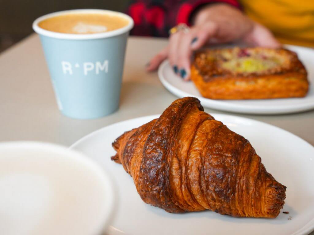 closeup of croissant, coffee and danish being grabbed by a hand