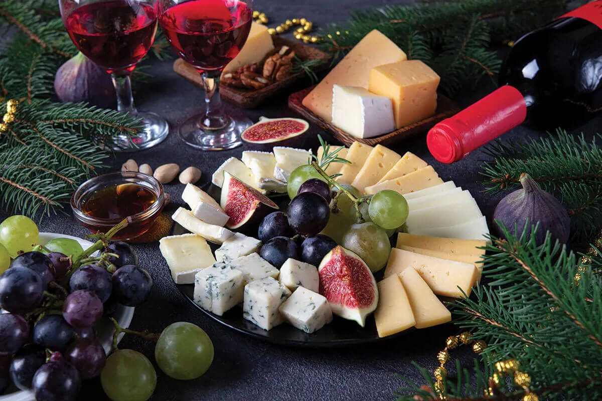 Plated selection of cheese, grapes, nuts, and accompaniments with glasses of red wine