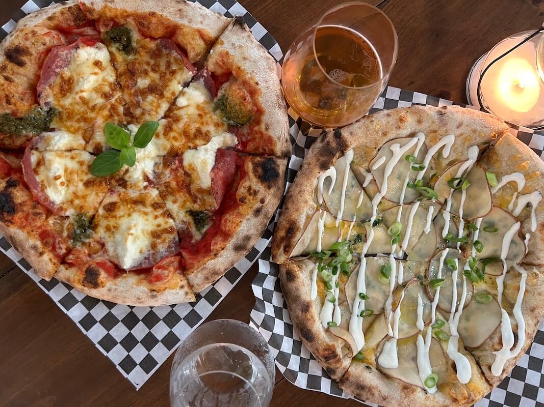 overhead shot of two wood fired pizzas at Elgin Harvest with two drinks