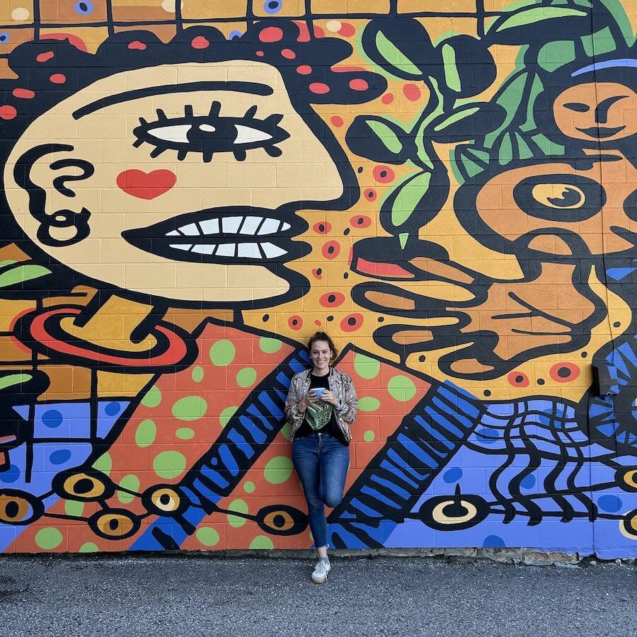 gabby holding a coffee in front of Andrew lewis mural