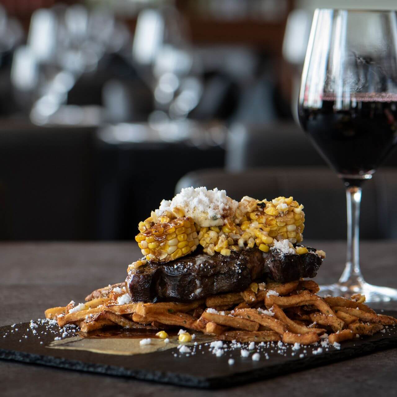 photo of steak topped with corn and fries underneath and a glass of red wine at cliffside at muskoka bay