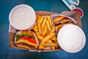overhead shot of two burgers fries and drinks in a box on blue table