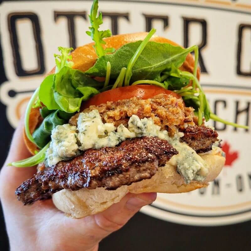 hand holding the blue cheese bacon burger at otter creek kitchen