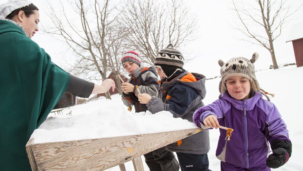 little kids eating maple taffy from a snow table
