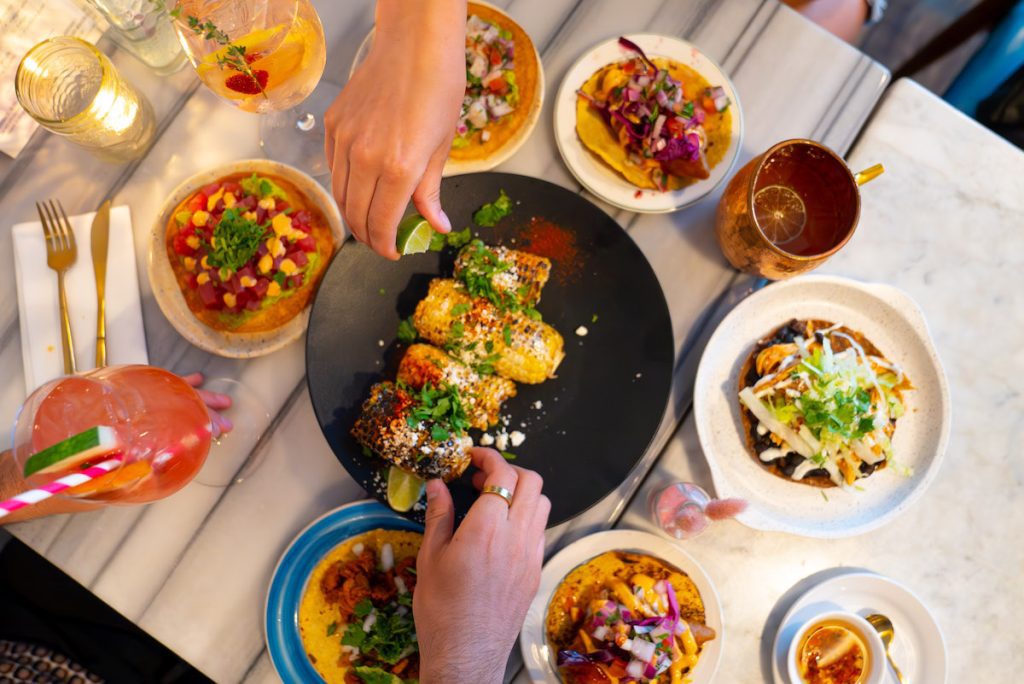overhead shot of two hands squeezing lime on corn and a spread of food at La Condesa