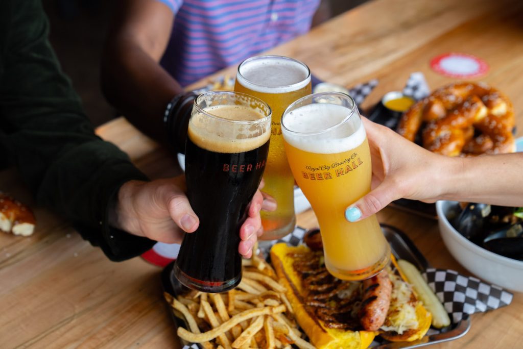 Three arms from Ian, Royden and Gabby cheersing beer over food at Royal City Brewing Co.