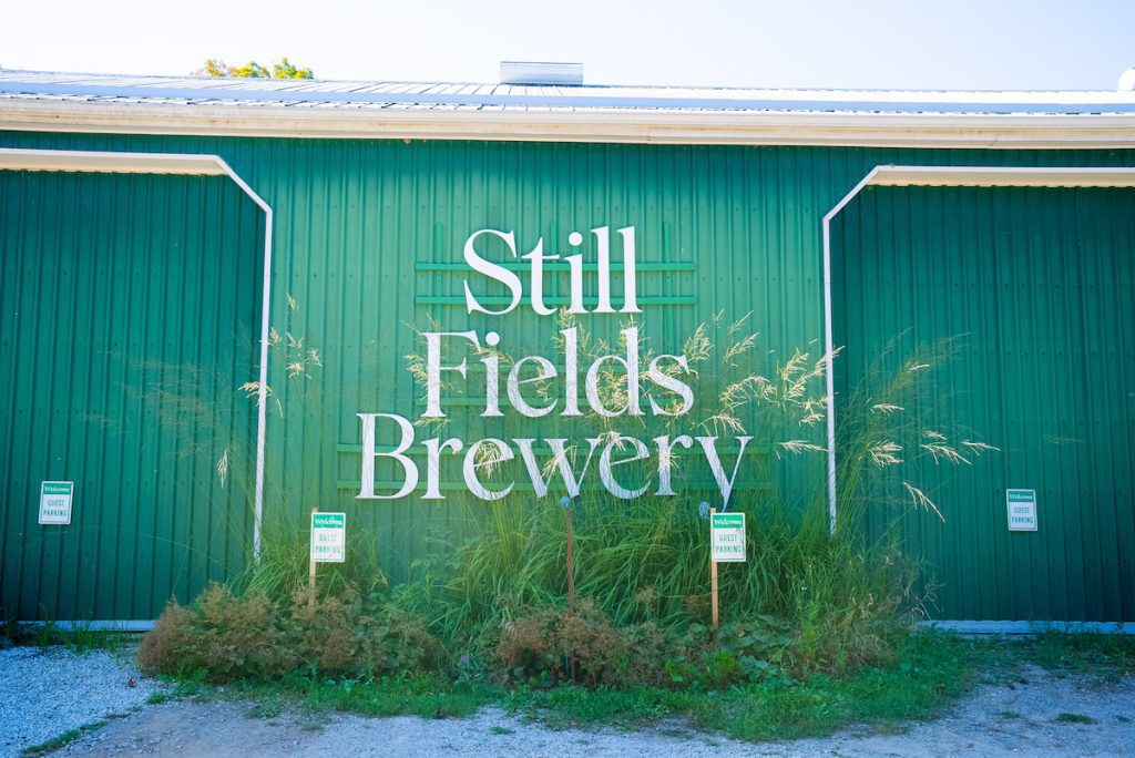 Exterior shot of the Still Fields Brewery sign on the side of a bright green barn