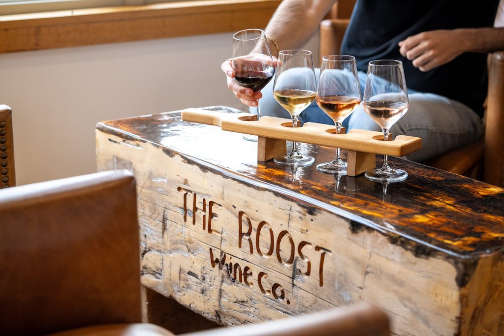 close up shot of the table at the roost with a sampling of wine on top and a hand reaching toward it
