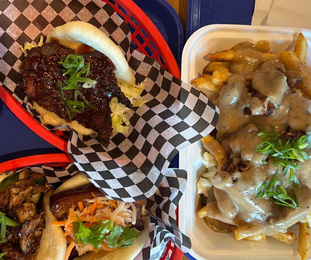 overhead shot of two baos and duck poutine on checkered paper