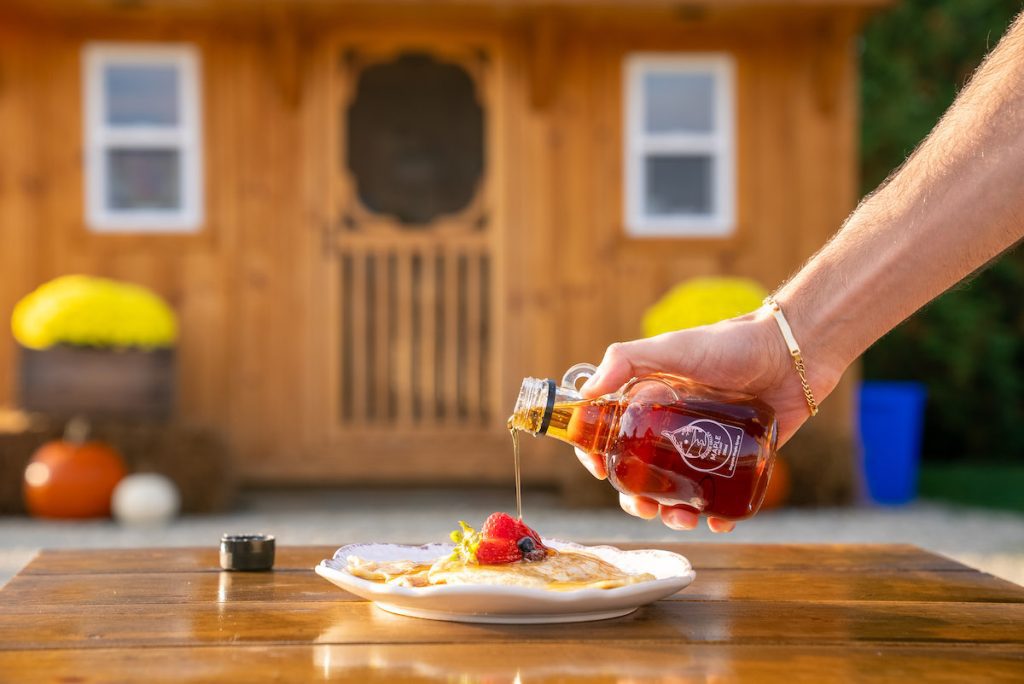 maple syrup being poured over pancakes and fruit outside one of the cabins at boho beaver