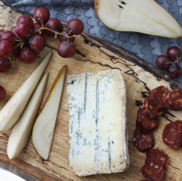 overhead shot of highland blue cheese on a board with some grapes and a pear