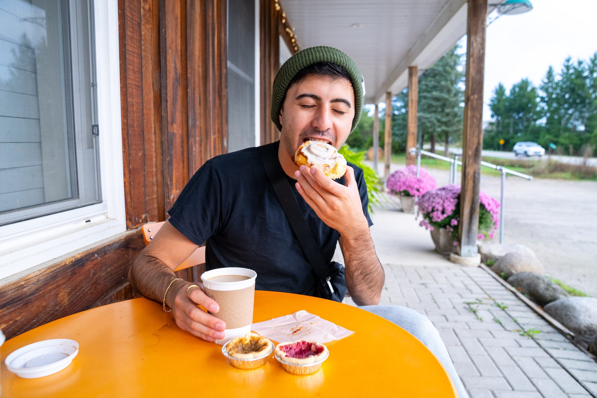 zain taking a bite of a cinnamon bun at an orange table outside of Ravenna Country Market
