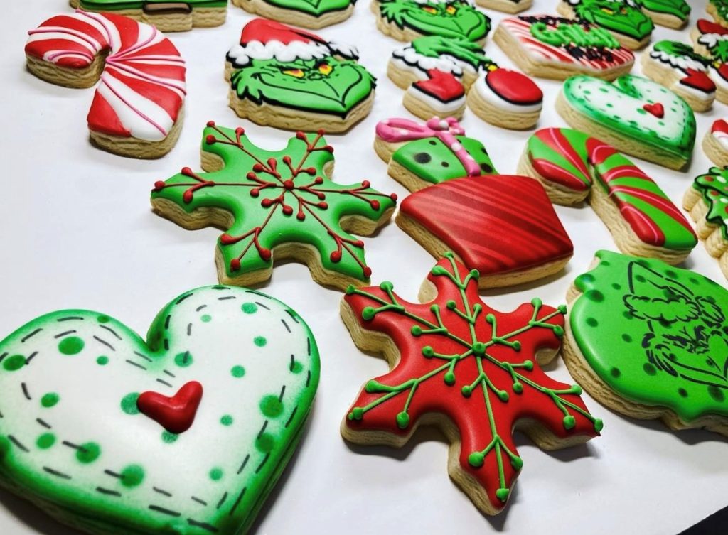 holiday themed cookies in green, white and red shaped like hearts, snowflakes, the grinch and more
