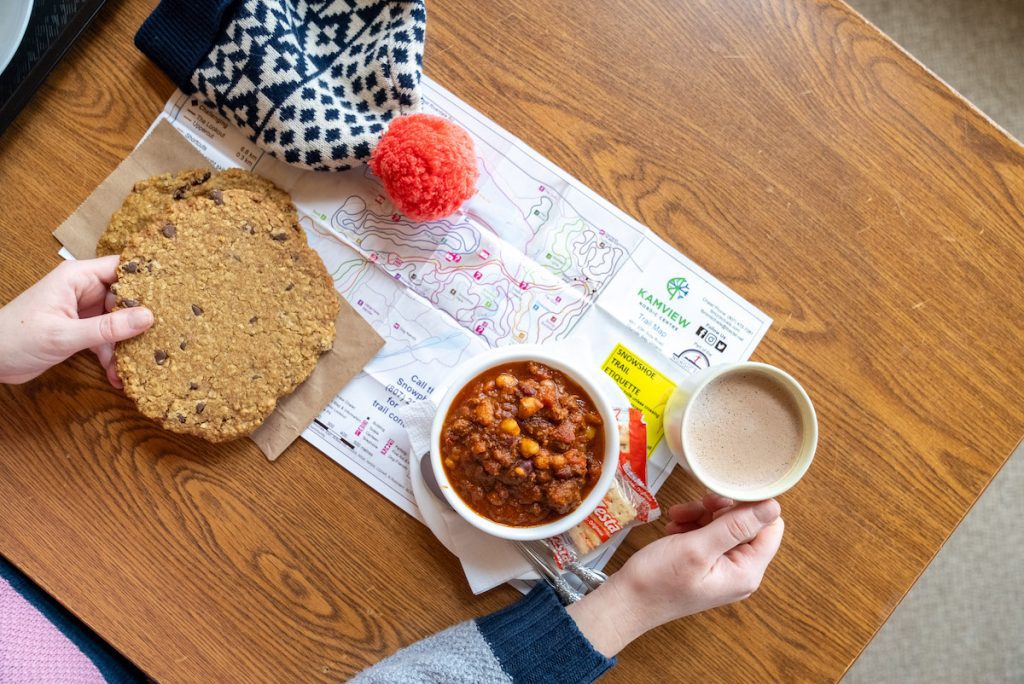 Overhead shot of a trail map at Kamview, cup of coffee, bowl of chilli, giant cookie and a touque.