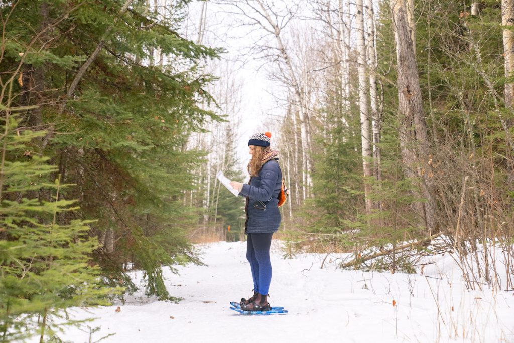 Girl reading a map wearing snow shoes on a trail at Kamview Nordic Centre.