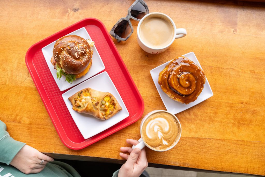 overhead shot of breakfast sandwich, breakfast ray, sticky bun. cappucino and coffee at Sweet North