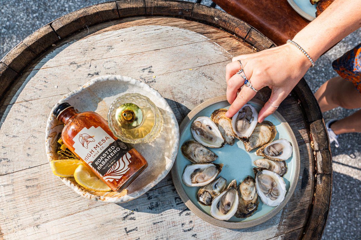 overhead shot of hand reaching into grab an oyster next to a bowl of hot sauce