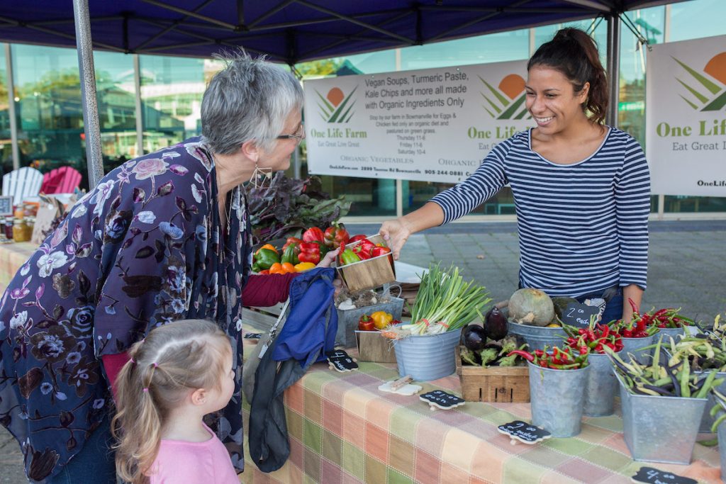 woman handing fresh produce to another woman at the farmers' market