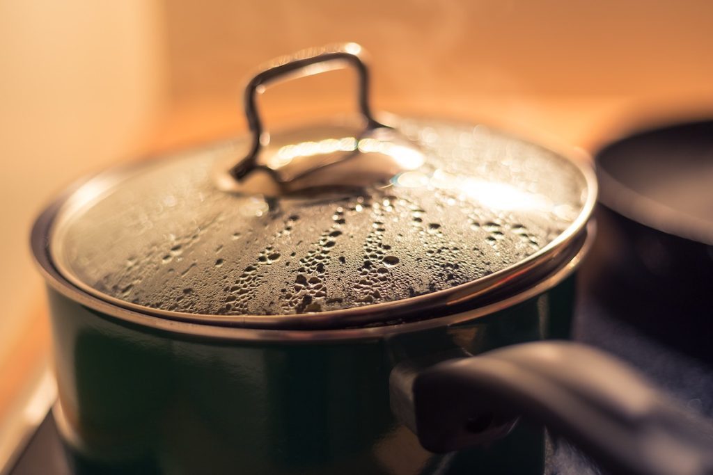 close up of a pot on the stove with a handle and steamed up lid