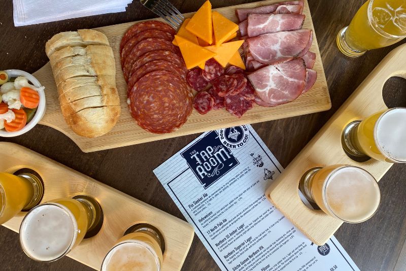 Close up image of a charcuterie board with flights of 3 beers with a taproom menu showing.