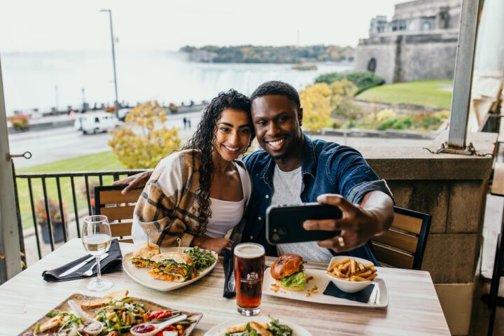 Couple taking a selfie at their table at Queen Victoria Place overlooking the falls