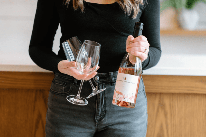 shot of woman holding glasses and rosé wine bottle.