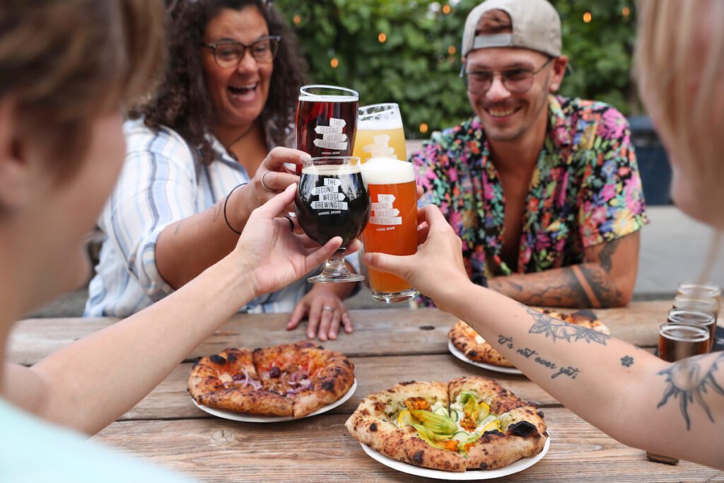 People cheersing beers over pizza at second wedge