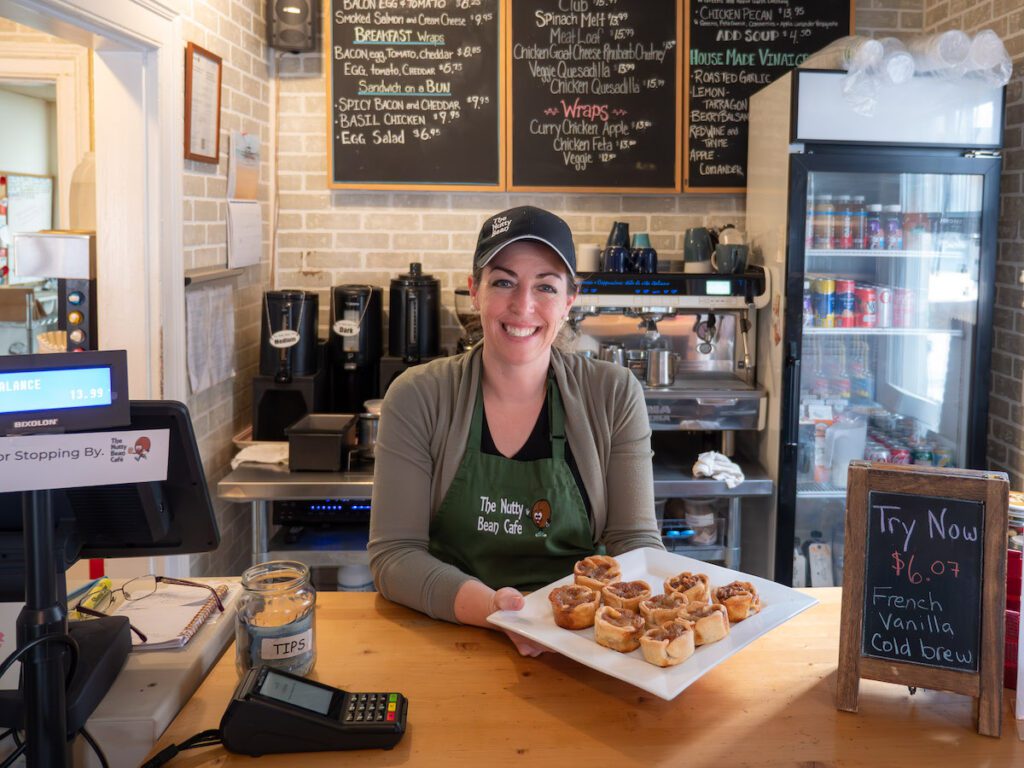 Woman holding a tray of butter tarts at the nutty bean cafe behind the counter