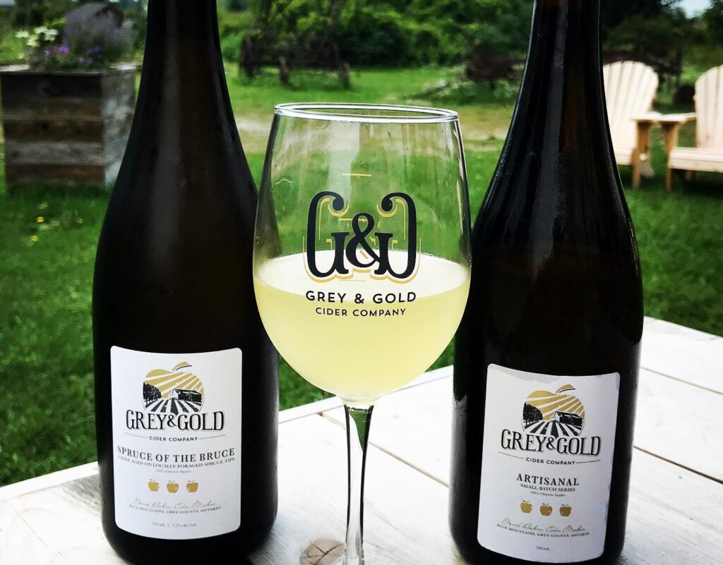 one glass and two bottles of grey and gold cider 