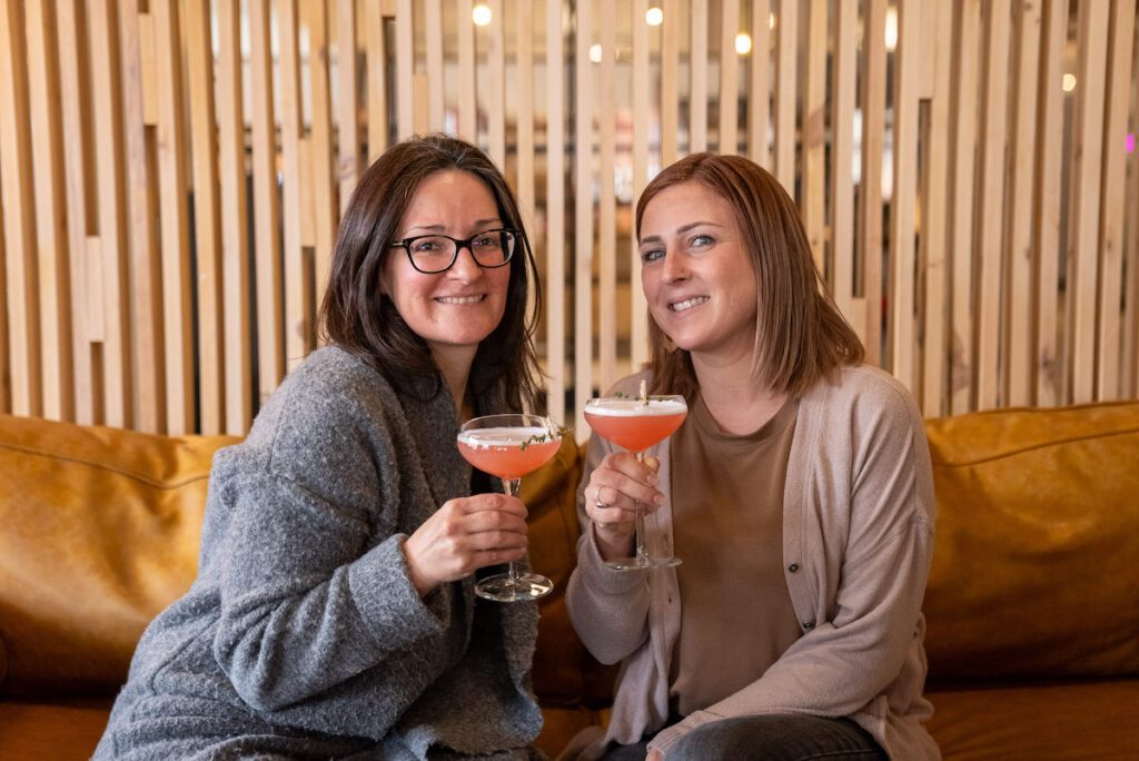 Two women drinking Turn Back Thyme cocktails at Woodside Bar inside of Goods n' Co