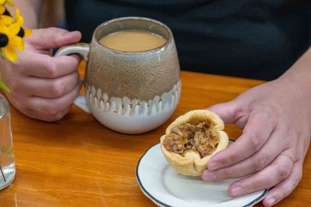 hands holding a butter tart and cup of coffee at Hidden Goldmine Bakery