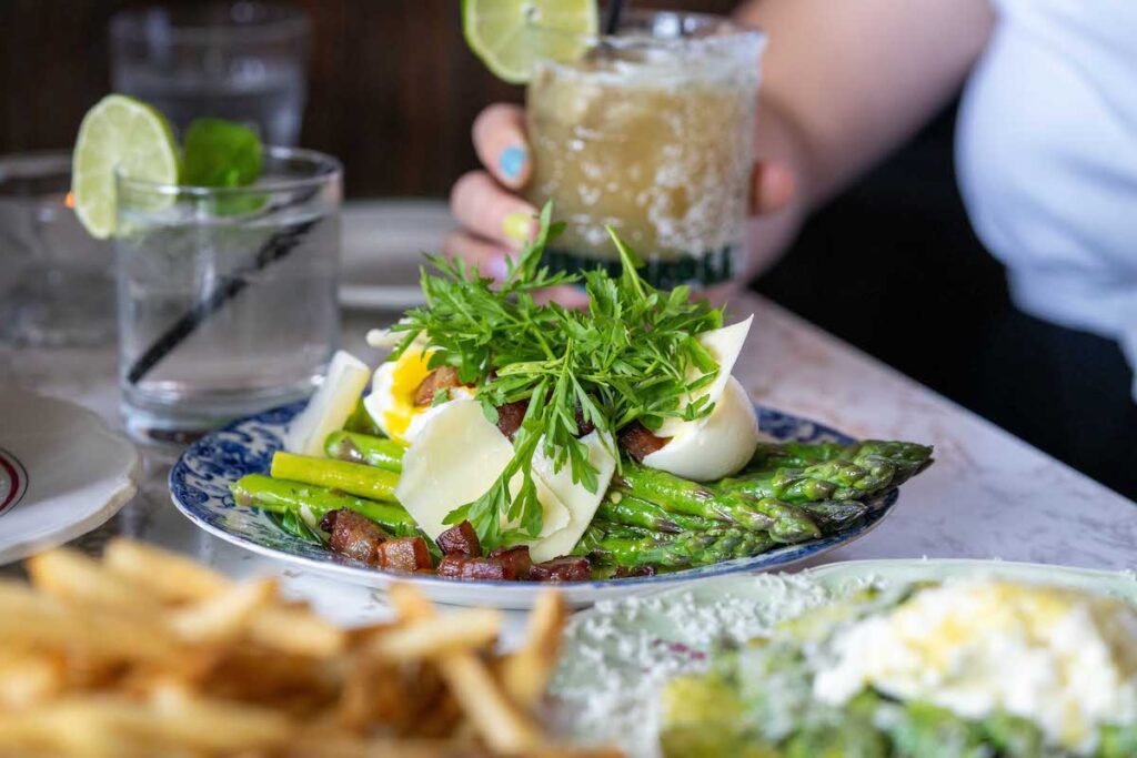 shot of the asparagus lyonnaise and cocktail in the background