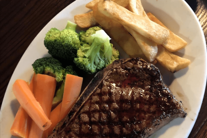 close up of plate with vegetables, grilled steak, and french fries.