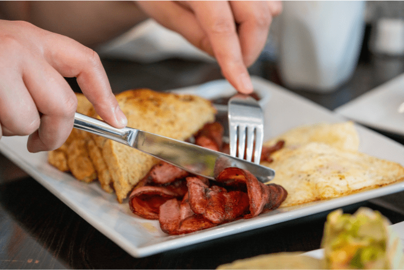 Close up of fork and knife cutting bacon on breakfast plat served at Kitchen Kuttings Cafe