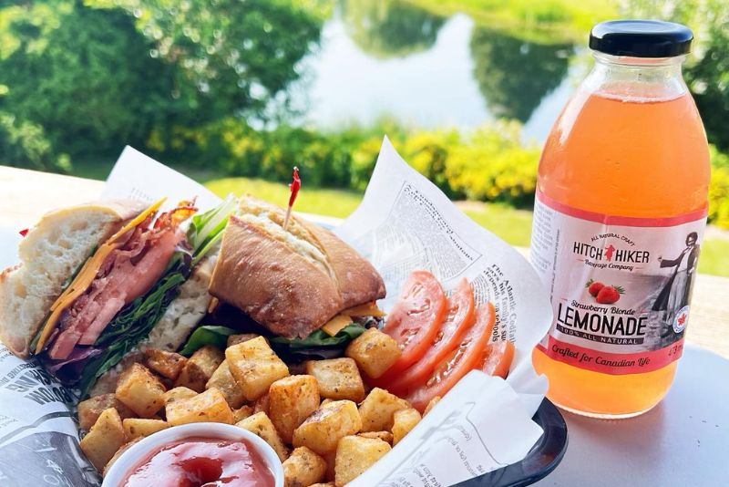 Close up image of sandwich served with cubed potatoes and a glass bottle of strawberry lemonade.