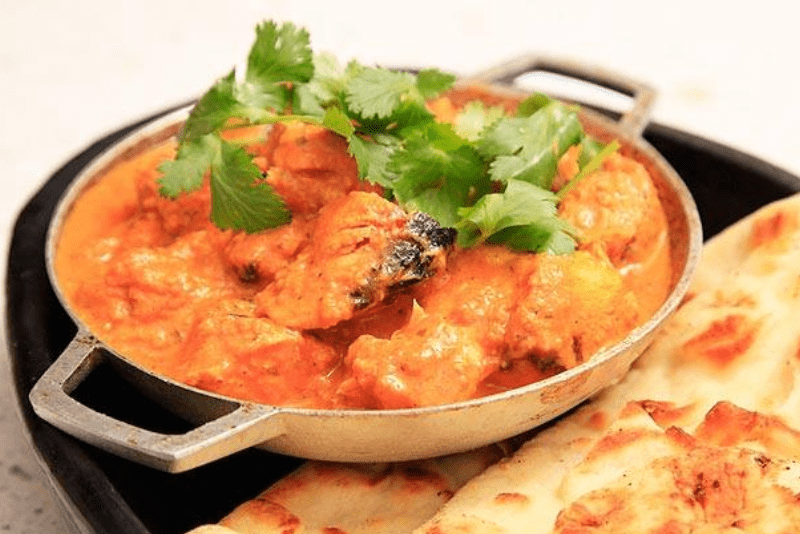 plate of butter chicken and naan bread on the side of the plate.