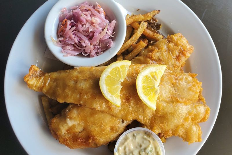 Close up of battered fish and chips dish with lemon slices and sauce ramekin