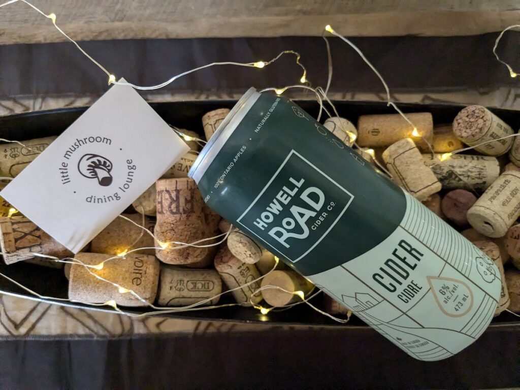 overhead shot of can of howell road cider in green and a little mushroom dining lounge card