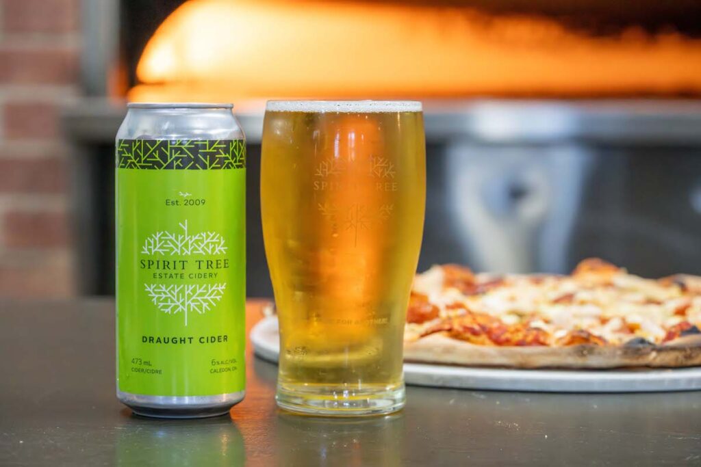 photo of spirit tree can, pint in a glass and wood fired pizza in the background